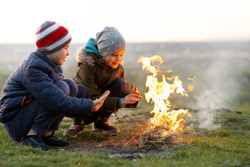 Two children playing with fire outdoors in cold weather.