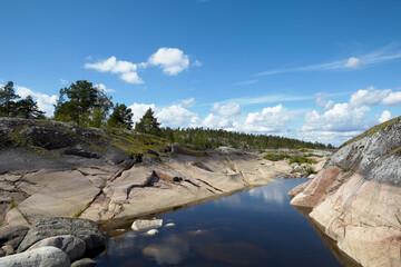 Ladoga lake. Island. Among the granite ledges is a small lake. Clouds are reflected in the water. Blue sky.
