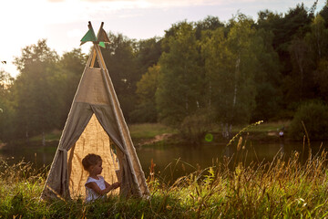 Girl at sunset in nature. Wigwam by the lake. New home in a hut. CHILDREN'S GAMES. High quality...