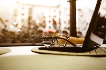 Modern glasses of businesswoman lying on notebook on table in cafe. Freelance working in restaurant. Business background. Flare copyspace for text and design