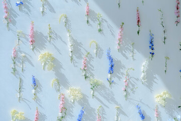 A lot of flowers of different colors fixed on a wall of white, blue, pink, yellow colors. Home decor background. Flower multicolored installation. Selective focus.