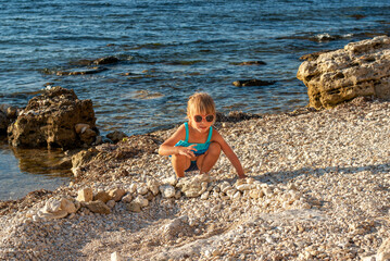 Baby girl in a blue swimsuit on a rocky seashore
