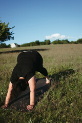 Outdoor yoga. Young overweight woman doing yoga exercise in the meadow. Open air workout, healthy lifestyle, weight loss