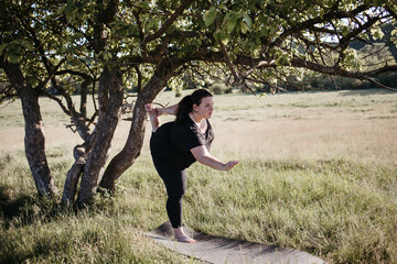 Overweight woman practicing yoga outdoors exercising on fitness mat in nature. Yoga for beginners. Weight loss