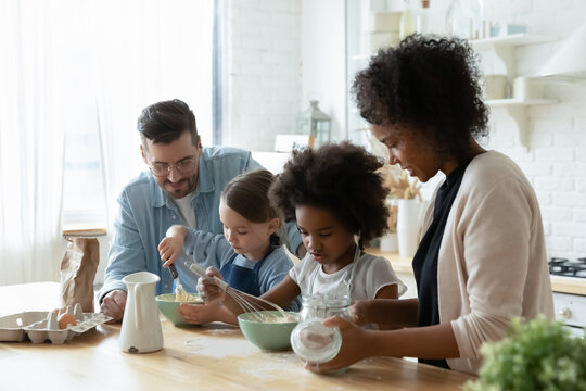 Little helpers and parents cook pie together in kitchen making cookies or morning pancakes, mother teach small daughters share experience and family recipes, hobby and good pastime activity concept - Powered by Adobe