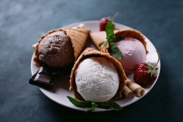 Ice cream set of strawberry, chocolate and vanilla flavored scoops in waffle cones on white plate, close up. Delicious summer snacks
