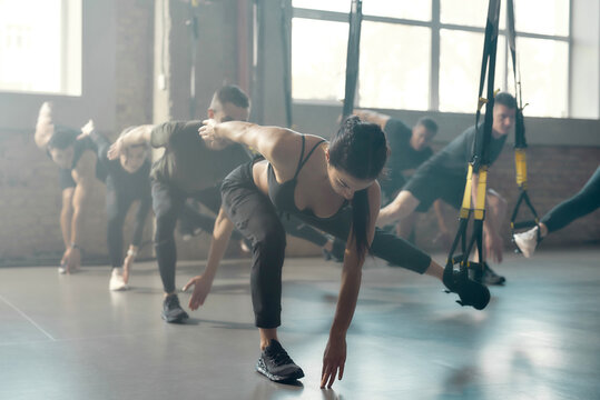 Fitness Center. Portrait of men and women doing fitness training exercises at industrial gym. Straps, group workout concept