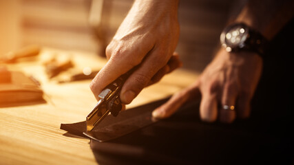 Working process of the leather belt in the leather workshop. Man holding tool. Tanner in old tannery. Wooden table background. Close up man arm. Warm Light for text and design. Web banner size
