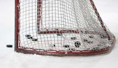 An ice hockey goal with mesh net and pucks inside standing on ice.