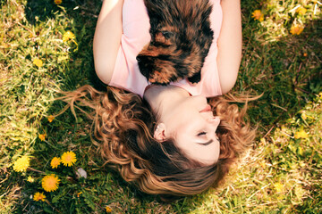 Girl lying on grass with cat on chest. Spring or summer warm weather concept. Bokeh background. Ginger kitten with two face color mask