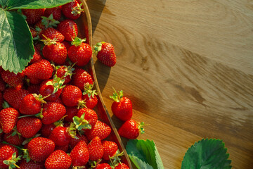 A lot of strawberries with leaves scattered on a wooden table, closeup background top view