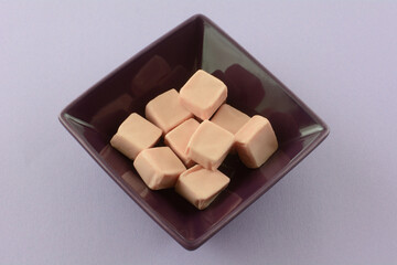 Strawberry toffee candy squares in purple candy bowl on lavender background