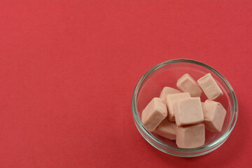 Strawberry toffee candy squares in glass candy bowl on red background