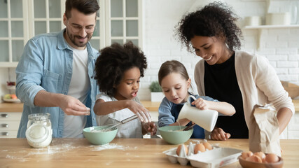 Full multi ethnic family with adorable daughters gathered in modern kitchen cooking pancakes...