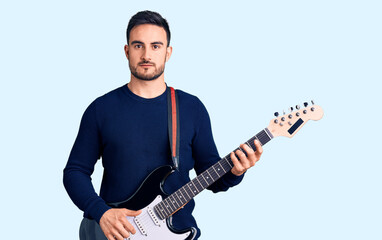 Obraz premium Young handsome man playing electric guitar thinking attitude and sober expression looking self confident