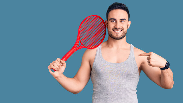 Young handsome man holding tennis racket pointing finger to one self smiling happy and proud