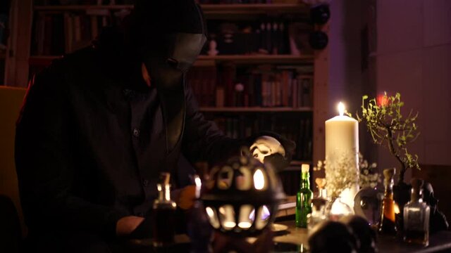magician in a crow mask sets fire to matches and man's skull