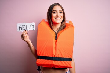 Young beautiful brunette woman wearing lifejacket holding paper with help word message with a happy...