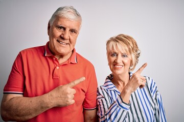 Senior beautiful couple standing together over isolated white background with a big smile on face, pointing with hand finger to the side looking at the camera.