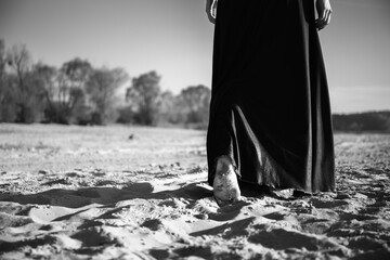 A woman walks into the distance on the sand with her bare feet. Black and white photo of a part of a person's body with a mood of depression, anxiety, sadness and loss.