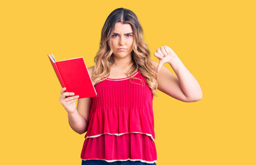 Young caucasian woman holding book with angry face, negative sign showing dislike with thumbs down, rejection concept