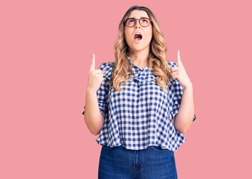 Young caucasian woman wearing casual clothes amazed and surprised looking up and pointing with fingers and raised arms.