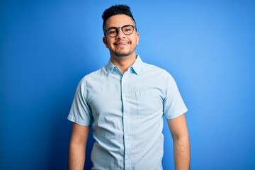 Fototapeta premium Young handsome man wearing casual summer shirt and glasses over isolated blue background with a happy and cool smile on face. Lucky person.