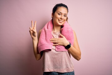Young beautiful brunette sportswoman wearing sportswear and towel over pink background smiling...