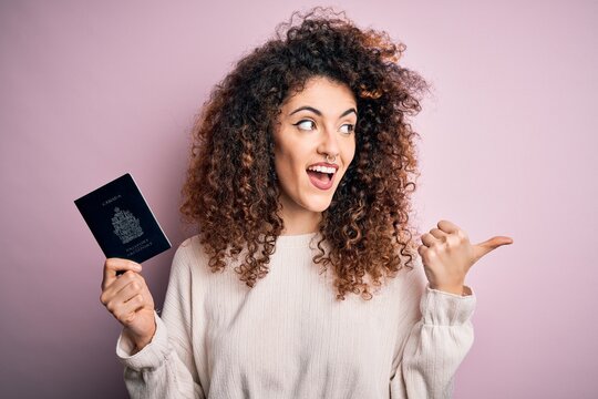 Beautiful tourist woman with curly hair and piercing holding canada canadian passport id pointing and showing with thumb up to the side with happy face smiling