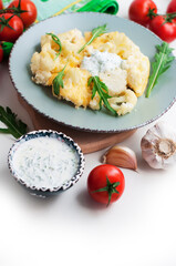 Baked cauliflower and tomatoes with cream-garlic sauce on white background