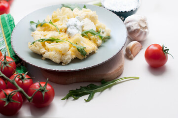 Baked cauliflower and tomatoes with cream-garlic sauce on white background