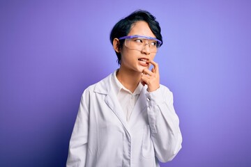 Young beautiful asian scientist girl wearing coat and glasses over purple background with hand on chin thinking about question, pensive expression. Smiling with thoughtful face. Doubt concept.