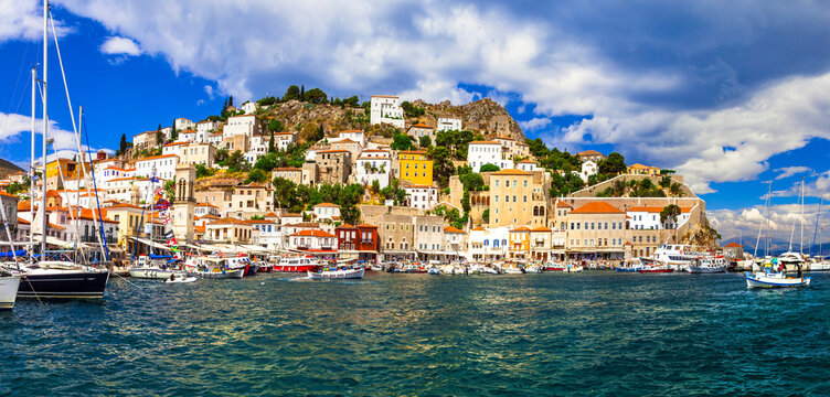 Greece Hydra island port with dramatic sky and colorful stone houses cascading to the sea. High resolution panorama Mediterranean aesthetics luxury yachts in Saronic Gulf Aegean summer vacation