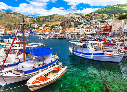 Greece authentic Hydra island port with colorful fishing boats and crystal clear turquoise sea. High resolution panorama Mediterranean aesthetics traditional  houses on hill Saronic Gulf Aegean summer