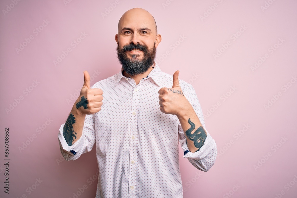 Poster Handsome bald man with beard wearing elegant shirt over isolated pink background success sign doing positive gesture with hand, thumbs up smiling and happy. Cheerful expression and winner gesture.