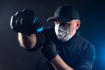 Fototapeta na wymiar Man stabs. Man in a medical mask on a dark background. Concept - the patient is engaged in sports. Resistance to the spread of infection. Concept - Humanity Strikes the Virus. Try defeat a pandemic
