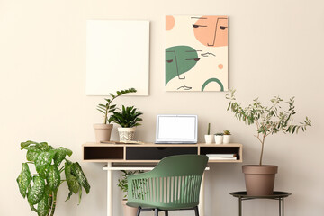 Obraz na płótnie Canvas Comfortable workplace with modern laptop and houseplants near light wall