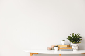 Green houseplants with aroma candles and books on table against light background