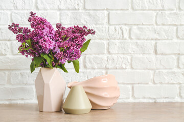 Vases with beautiful flowers on table near white brick wall