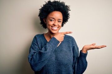 Young beautiful African American afro woman with curly hair wearing casual sweater amazed and smiling to the camera while presenting with hand and pointing with finger.