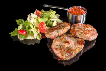 Delicious lamb meatballs served with fresh salad and mashed tomatoes with reflection, isolated on black background