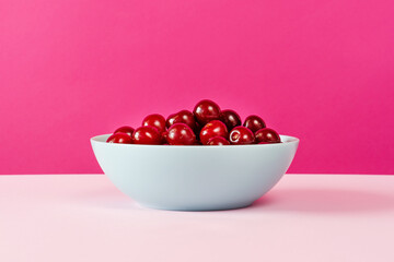 Ripe cherries in ceramic bowl on pink background front view copy space
