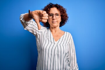 Middle age beautiful curly hair woman wearing casual striped shirt over isolated background looking unhappy and angry showing rejection and negative with thumbs down gesture. Bad expression.