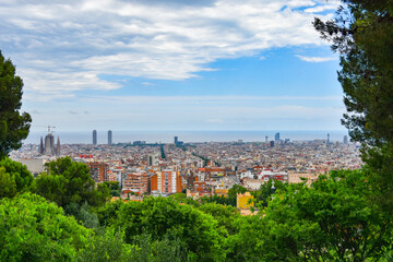 Fototapeta na wymiar Panoramic view of Barcelona cityscape framed with greenery and trees: plenty of buildings, houses, parks, and skyscrapers, residential and touristic districts, seascape on the horizon