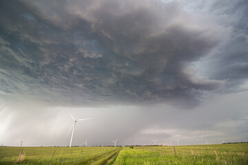 The dark base of a supercell thunderstorm over wind turbines in the prairie. Rain falls in the...