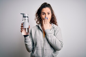 Beautiful woman with curly hair doing sport drinking bottle of water over white background cover mouth with hand shocked with shame for mistake, expression of fear, scared in silence, secret concept