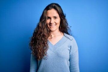 Young beautiful woman with curly hair wearing blue casual sweater over isolated background with a happy and cool smile on face. Lucky person.