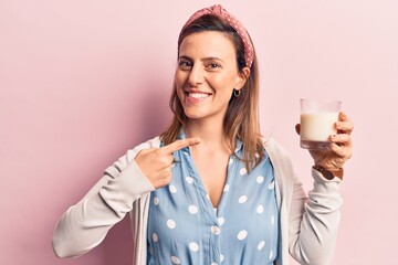 Young beautiful woman holding glass of milk smiling happy pointing with hand and finger