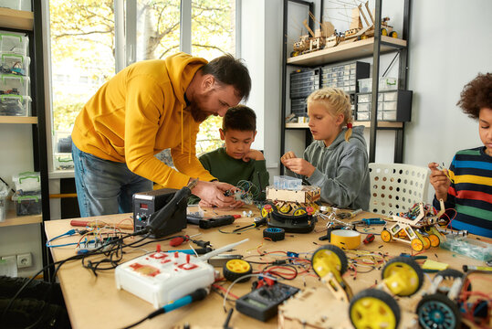 Solution to all problems. Young technicians building a robot, working with a wiring kit together with a male teacher at a stem robotics class. Inventions and creativity for kids