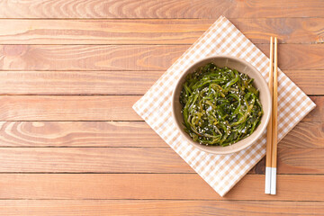 Bowl with tasty seaweed and chopsticks on wooden background